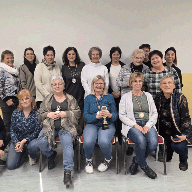 Gruppenfoto von 20 Frauen, lächelnd, in einem Raum, einige halten Trophäen.